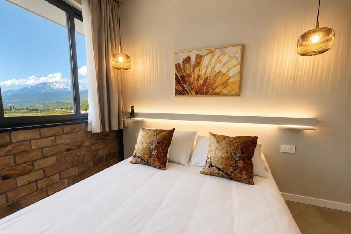 Habitación de hotel con una cama grande, dos almohadas, una obra de arte en la pared y vistas de una montaña a través de una ventana.