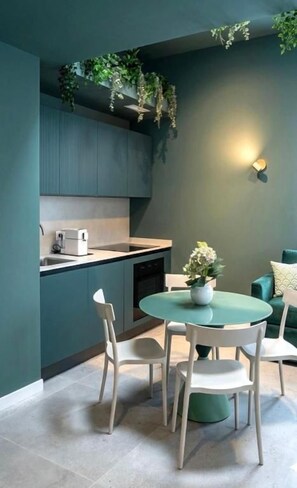 Una cocina moderna con comedor, que incluye una mesa redonda con sillas, horno empotrado y una planta colgante.