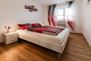 A bedroom with a bed, bedside table, lamp, and a window with curtains. - Holiday apartment with 2 bedrooms (Fischen im Allgäu)