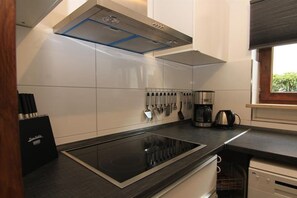 Une cuisine moderne dotée d’une plaque de cuisson intégrée, d’appareils électroménagers en acier inoxydable et d’une fenêtre laissant entrer la lumière naturelle.