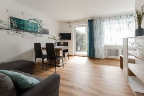 Ein modernes Wohnzimmer mit einer Couch, einem Essbereich mit Stühlen, einem Fernseher und einem Fenster mit Vorhängen.