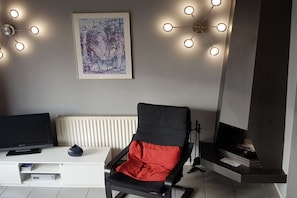 A living room with a black armchair, a white entertainment unit, a fireplace, and a framed abstract painting. - LeNo at Center Parcs (Butjadingen)