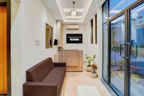 A reception area with a sofa, a sign indicating it's a serviced townhouse, and a view through a glass door. - Townhouse Indore Ring Road (Indore)