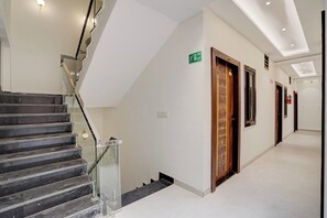 Pasillo de hotel con escalera de barandilla de vidrio, señal de salida de incendios y puerta con diseño geométrico.