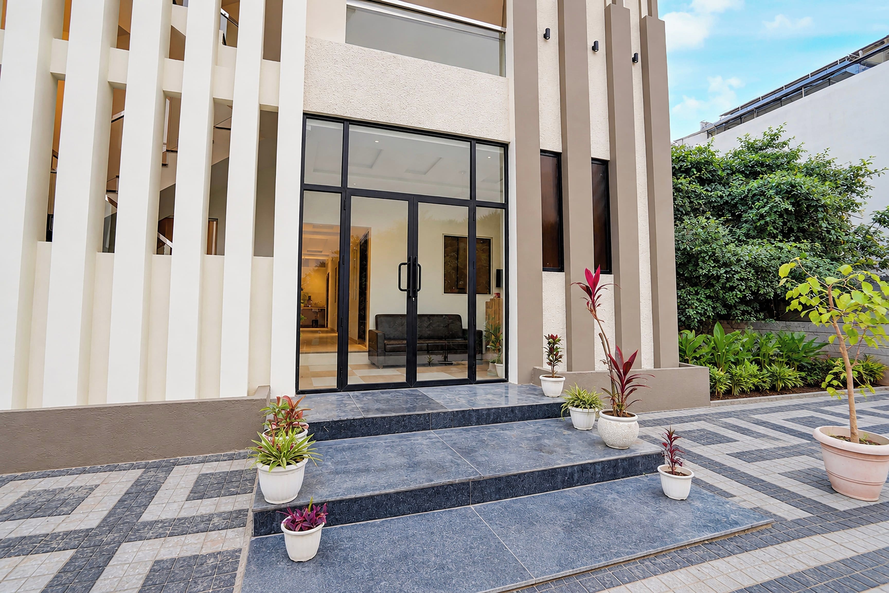 Un edificio moderno con entrada de vidrio, plantas en macetas y un patio con baldosas.