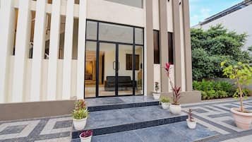 Un edificio moderno con entrada de vidrio, plantas en macetas y un patio con baldosas.
