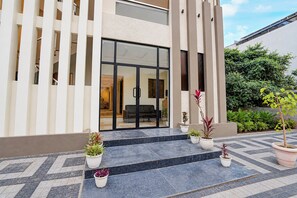 Un edificio moderno con entrada de vidrio, plantas en macetas y un patio con baldosas.