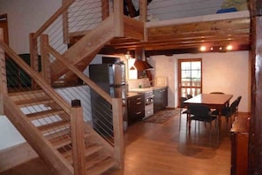 Een houten trap leidt naar een hoger gelegen ruimte met een keuken en een eethoek.