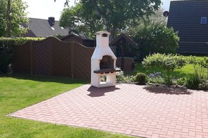 Een met bakstenen bestrate terras met een witte buitenoven in een tuin.