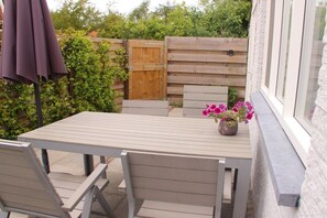 Eine Terrasse im Freien mit Tisch und Stühlen, einem Holzzaun und einem Blumentopf mit rosa Blüten.