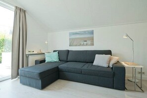 A modern living room with a sectional sofa, a small table, and a floor lamp. - Holiday apartment with 1 bedroom (Oostkapelle)