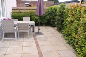 An outdoor patio with a table and chairs, a purple umbrella, and a hedge. - Holiday apartment with 1 bedroom (Oostkapelle)