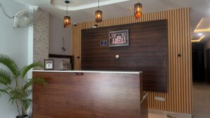 A reception desk with a wooden finish, a wall-mounted fan, and decorative lighting fixtures. - Collection O Vijay Nagar Square Indore (Indore)