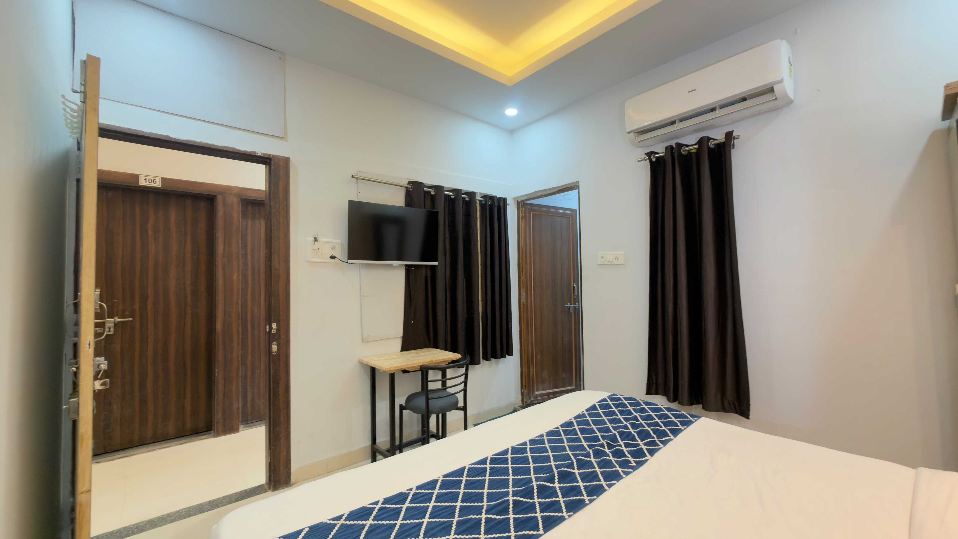Una habitación de hotel con cama, escritorio, televisión y aire acondicionado.