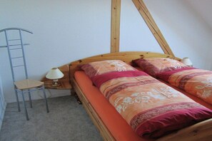 Quarto com cama de madeira, duas almofadas, mesa de cabeceira com abajur e uma cadeira.