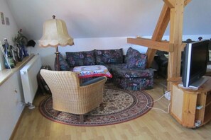 Uma sala de estar com sofá, uma poltrona, televisão sobre um suporte de madeira e um abajur.
