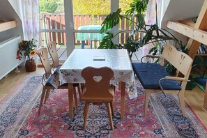 Een eetgedeelte met een tafel, stoelen en een bank. Er staan planten en er is uitzicht op het omliggende landschap.