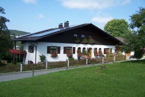 A white building with a dark roof, multiple windows, and a wooden fence in front. - Holiday apartment with 1 bedroom (Teisnach)