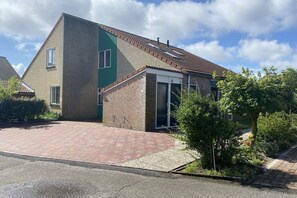 Un immeuble résidentiel de deux étages avec une façade en briques, un mur d’accent vert et une allée pavée.