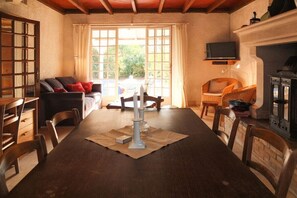 A dining area with a wooden table, chairs, a fireplace, and a television mounted on the wall. - "Le Bateau" by the sea (Vandays Montalivet)
