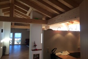 A room with wooden beams, a kitchen area with a sink, and a view of a balcony with chairs. - Holiday apartment in Seeg with swimming pool (Seeg)