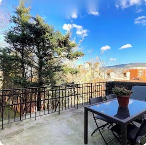 A balcony with a glass table and chairs, a potted plant, and a view of buildings and trees. - The San Giusto Terrace: A Haven of Peace in Trieste's Historic Center (Trieste)
