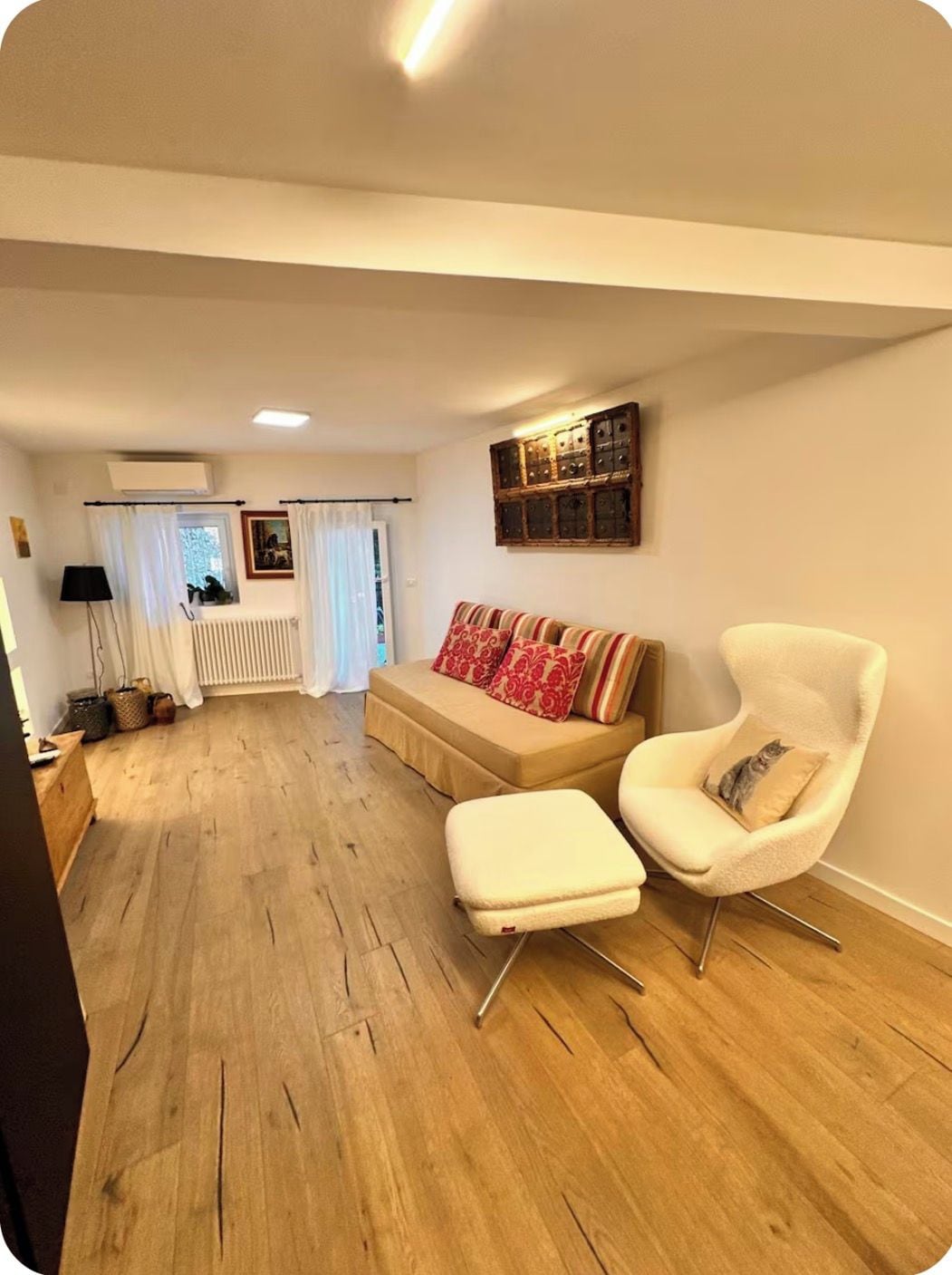 A living room with a sofa, armchair, and ottoman, wooden flooring, and a radiator.