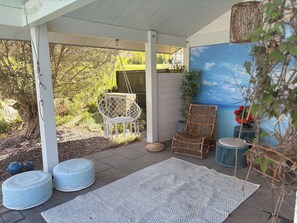 A covered outdoor seating area with a white ceiling, a hanging chair, a rattan chair, two round ottomans, and a rug. - Architect-designed home with a heated pool, just a stone's throw from Geneva and the ski slopes (Présilly)