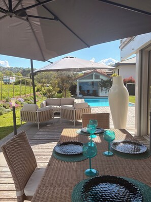 Une terrasse extérieure avec une piscine, des meubles en osier et un grand parasol.