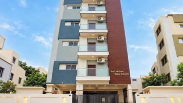 Un edificio residencial de varios pisos con balcones, unidades de aire acondicionado y una entrada protegida por una reja.