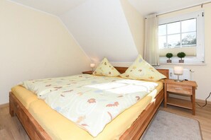 Ein Schlafzimmer mit einem Bett, einem Nachttisch, einem Fenster mit Vorhängen und einer kleinen Pflanze auf dem Fensterbrett.