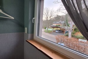 Ein Zimmer mit Fensterblick auf eine Wohngegend, einem Holzbodenregal und einem an der Wand montierten Lichtschalter.