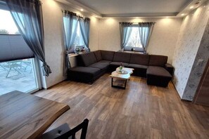 A modern living room with a sectional sofa, a coffee table, and a dining table. - Holiday home with 1 bedroom (Blankenburg)