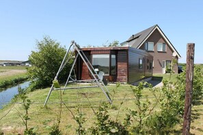 A modern house with a large window, a satellite dish, and a wooden deck. - Cabin in Julianadorp with swimming pool (Julianadorp)