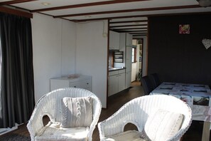 A room with two wicker chairs, a small table, a kitchenette, and a dark wall with a heart decoration. - Cabin in Julianadorp with swimming pool (Julianadorp)
