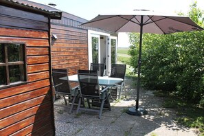 A wooden cabin with a patio table and chairs, an umbrella, and a door leading to an outdoor area. - Cabin in Julianadorp with swimming pool (Julianadorp)