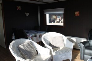Une pièce comprenant une table à manger, deux chaises en osier, un fauteuil en cuir noir et une fenêtre avec des stores.