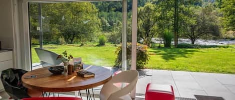 A modern dining area with a table and chairs, a red bench, and a view of a lush garden through large glass doors.
