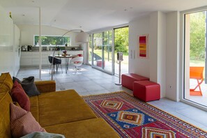 A modern living room with a sofa, a coffee table, and a dining area with chairs. There is a large window providing a view of the outdoors. - View of the Sieg River (Windeck)