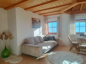 Un salon confortable avec un canapé, une table à manger et des chaises, un tableau accroché au mur et une fenêtre avec des rideaux.