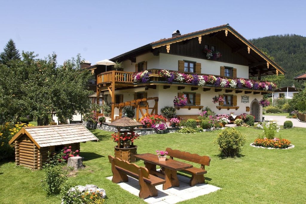 A traditional chalet with a balcony adorned with flowers, a wooden bench, and a small garden.