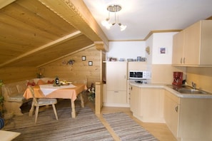 A cozy kitchen with wooden beams, a dining area with a table and chairs, and a small refrigerator. - Guesthouse on the Großwaldbach (Inzell)