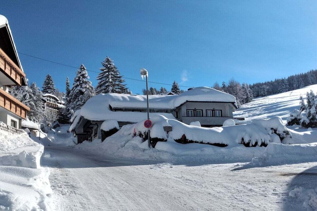 A snow-covered building with a clear sky, surrounded by snow-covered trees and a clear road.
