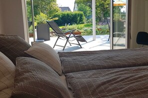 A bedroom with a large bed, a view of the garden through a sliding glass door, and a chair outside. - Holiday apartment SEElig (Überlingen - Nußdorf)