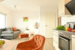 Une cuisine moderne dotée d’un four encastré et d’un coin repas avec un canapé gris et un fauteuil orange.