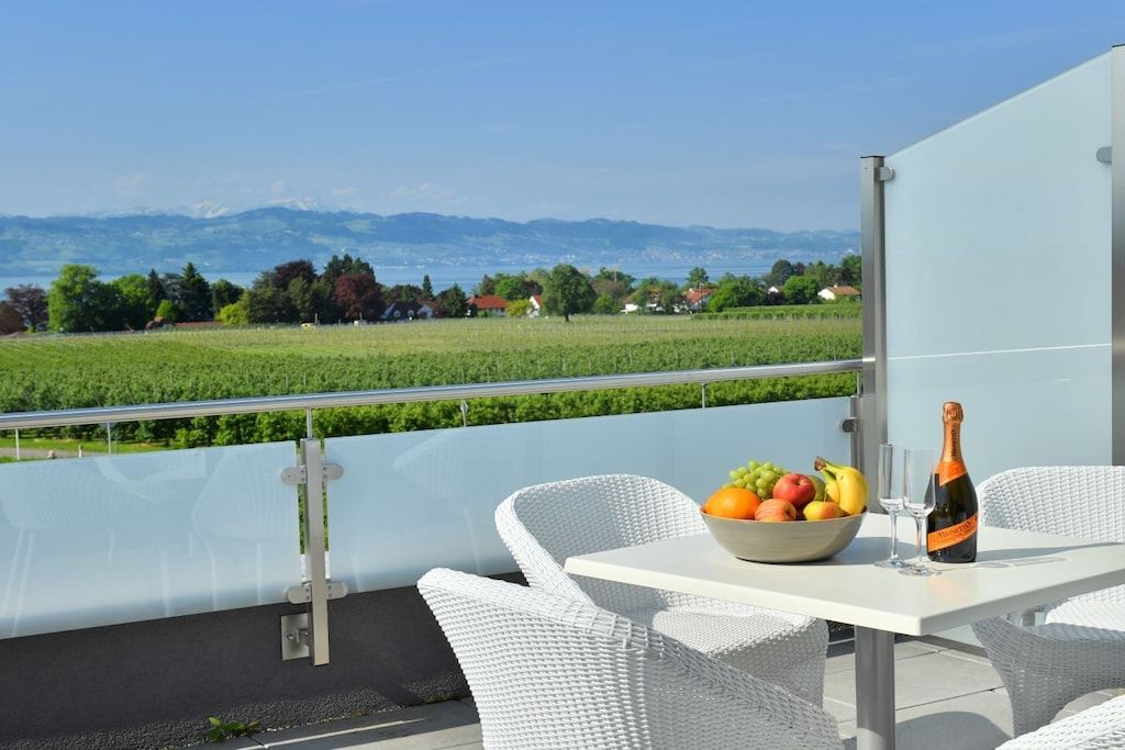 Een balkon met een tafel gedekt voor twee personen, een schaal fruit en een fles champagne.