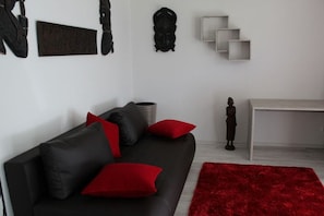 A modern living room with a black sofa, red cushions, a red rug, and decorative items on the wall. - Holiday apartment in Waren with swimming pool (Waren)