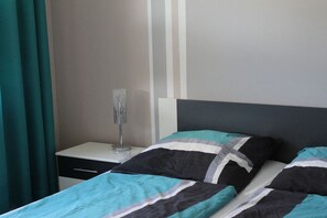 A bed with a striped bedspread and pillows, a bedside table with a lamp, and a wall with vertical stripes. - Holiday apartment in Waren with swimming pool (Waren)