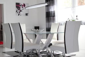 A modern dining area with a glass table surrounded by white chairs with black accents. - Holiday apartment in Waren with swimming pool (Waren)