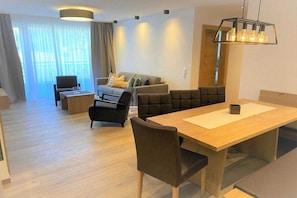 Un salon moderne comprenant un canapé, des fauteuils, une table à manger et une grande fenêtre avec des rideaux.